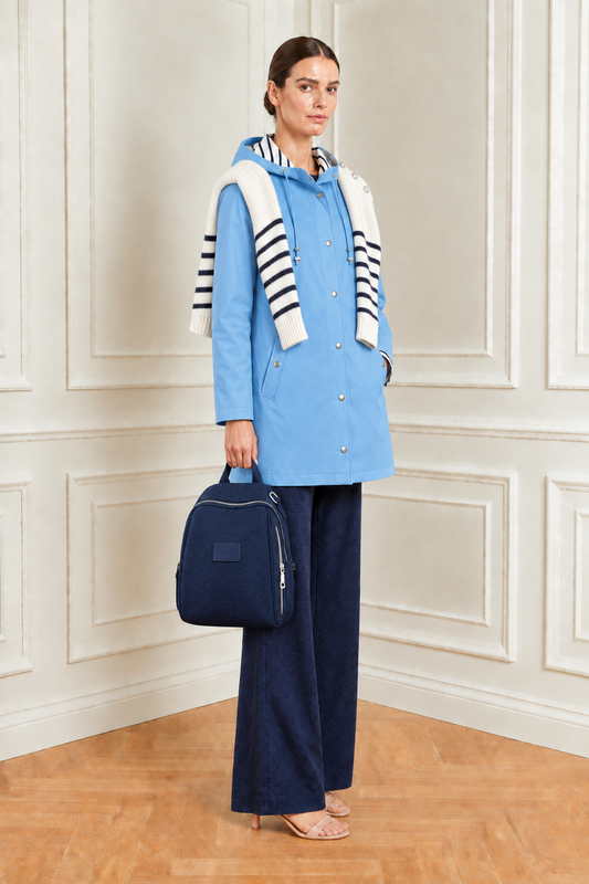 Modelo con chubasquero azul claro, mochila en la mano y jersey marinero sobre los hombros